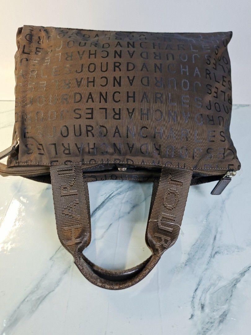 Charles Jourdan Brown Monogram Tote Handbag (Category: Tote Bags) located in Pasay City. Submitted by onick_79 (Listing ID 1468239079, Image 3). Description: - Brand: Charles Jourdan - Color: Dark Brown with all-over monogram letter print - Material: Durable nylon with matching hardware - Closure: Secure top zipper closure - Pockets: Roomy main compartment with a structured rectangular base and 1 exterior vertical zip pocket on the back - Straps: