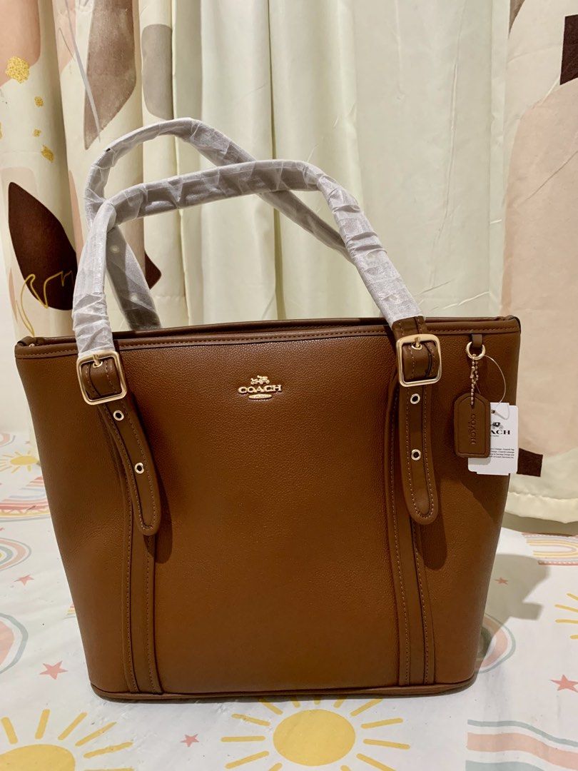 Coach Brown Leather Tote Bag (Category: Tote Bags) located in San Mateo. Submitted by trendsph_956 (Listing ID 1468280945, Image 1). Description: - Rich brown leather tote bag with elegant gold-tone hardware - Features the classic Coach logo stamped on the front - Double shoulder straps still wrapped in original protective paper (Brand New!) - Includes attached leather hangtag and interior tag on ball chain - Structured design with stylish vertic