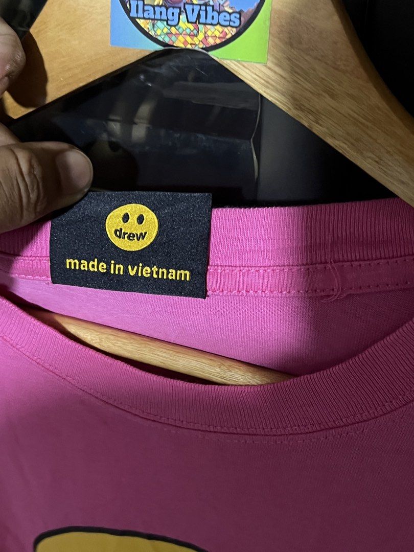 Drew House Pink Mascot SS Tee Size L (Category: Tshirts & Polo Shirts ) located in Davao. Submitted by thriftitemsss (Listing ID 1468196392, Image 3). Description: - Brand: Drew House - Item: Short sleeve tee - Color: Bright pink with iconic yellow smiley face graphic and black 'drew' lettering - Size: Large (verified by black collar tag) - Material: 100% cotton (interior care tag included) - Details: Ribbed crew neck collar, made in Vietnam, RN 