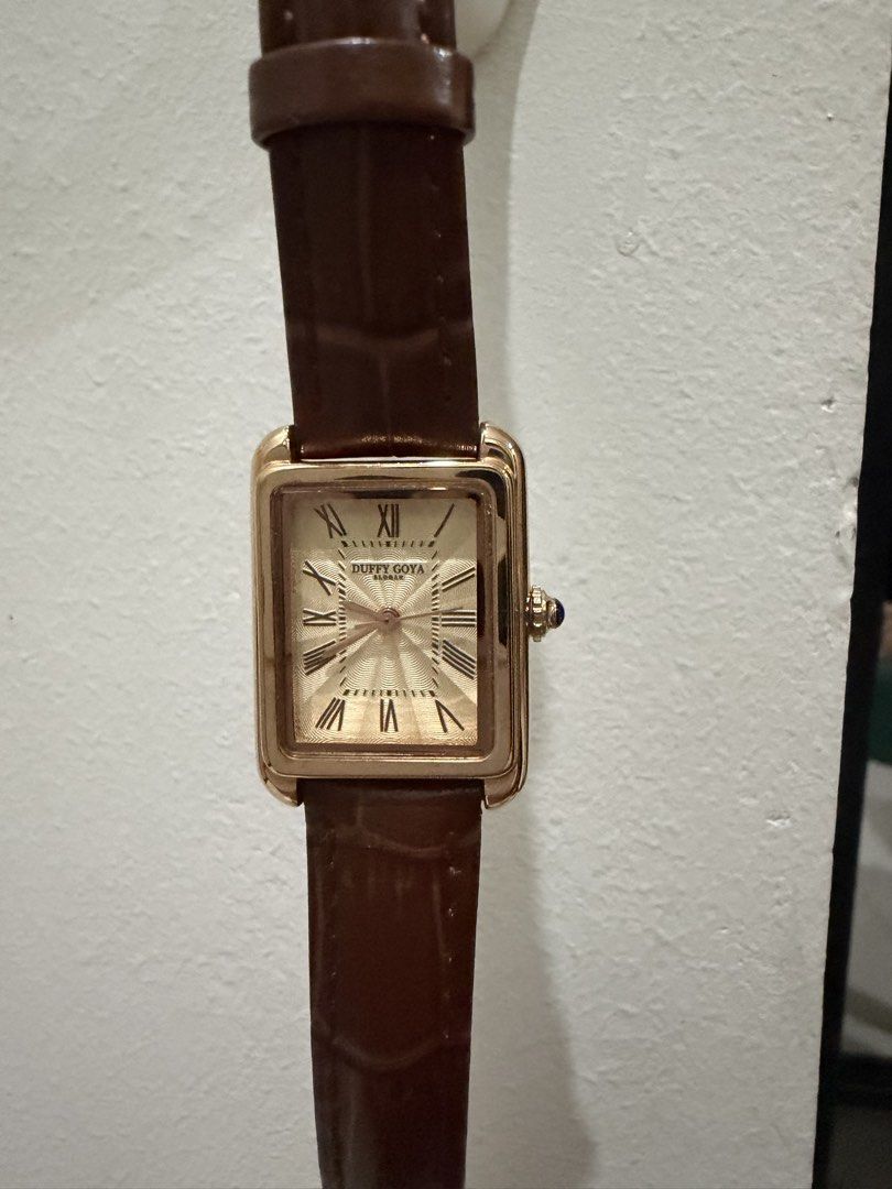 Duffy Goya rectangular gold dress watch brown strap (Category: Women's Watches) located in Pasay City. Submitted by gerlynnedc (Listing ID 1468211528, Image 2). Description: Duffy Goya dress watch with a rectangular gold case and textured dial. Roman numerals mark the hours. Blue cabochon stone set in the crown. Brown faux-croc leather strap with gold tone buckle. Clean crystal and polished metal finish. Classic vintage aesthetic, great daily pie