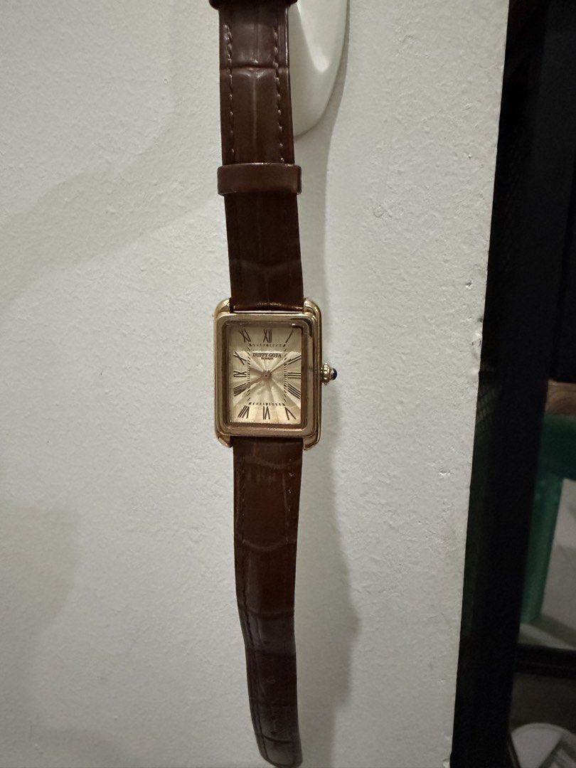 Duffy Goya rectangular gold dress watch brown strap (Category: Women's Watches) located in Pasay City. Submitted by gerlynnedc (Listing ID 1468211528, Image 1). Description: Duffy Goya dress watch with a rectangular gold case and textured dial. Roman numerals mark the hours. Blue cabochon stone set in the crown. Brown faux-croc leather strap with gold tone buckle. Clean crystal and polished metal finish. Classic vintage aesthetic, great daily pie
