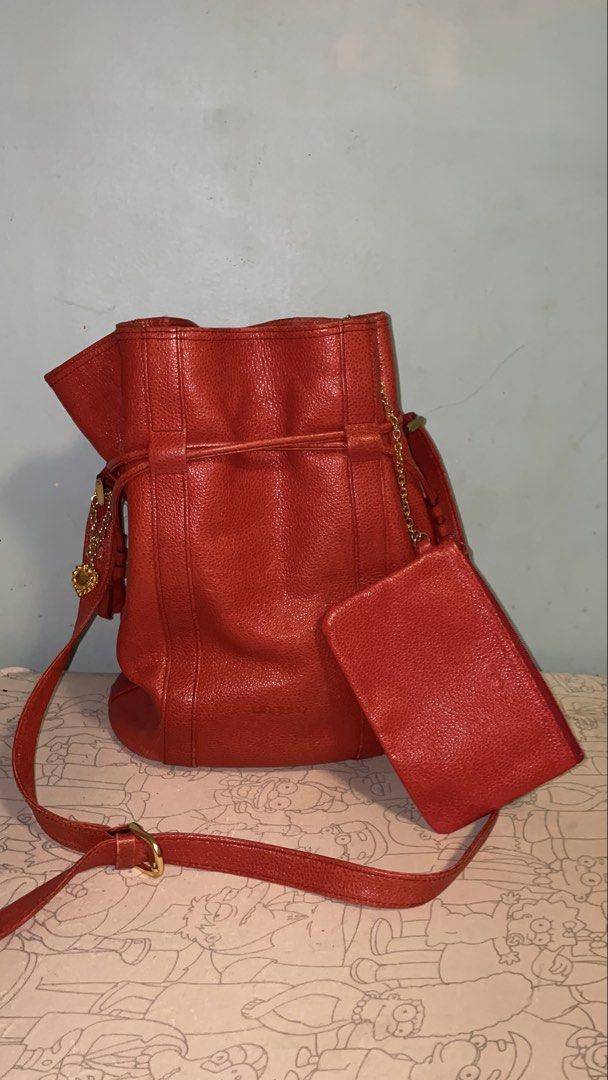 Emanuel Ungaro Red Leather Bucket Bag with Pouch (Category: Luxury Bags & Wallets) located in Manila. Submitted by ryoughhthrift (Listing ID 1468094732, Image 2). Description: - Brand: Emanuel Ungaro - Material: Premium textured leather in a bright red shade - Closure: Secure drawstring top - Strap: Adjustable shoulder strap for a custom fit - Bonus: Includes a matching detachable zippered pouch connected by a chic gold chain - Base: Flat oval ba