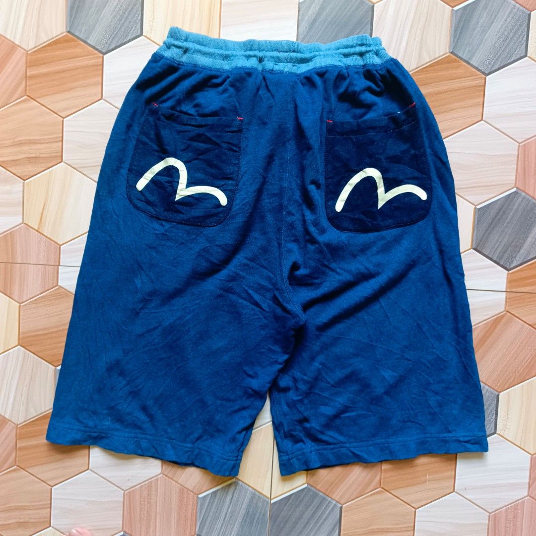 Evisu Blue Graphic Drawstring Shorts (Category: Shorts) located in Manila. Submitted by caps08 (Listing ID 1468257442, Image 3). Description: Deep blue shorts from Evisu. Elastic waistband with a drawstring closure for an adjustable fit. Contrasting red inner lining at the waist. Back pockets include embroidered graphic arcs. Front and lower legs feature distinct printed graphics including a round emblem and hexagonal kanji text. Soft fabric cons
