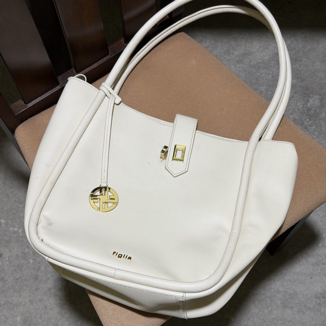 Figlia Jester Handbag Cream Color (Category: Shoulder Bags) located in Caloocan City. Submitted by catwonrideul (Listing ID 1468141321, Image 2). Description: - Brand/Model: Figlia Jester Handbag - Color: Cream - Original Price: ₱1,499 - Design: Structured with dual shoulder straps, gold-tone hardware, and front logo charm - Closure: Zip-top for security - Interior: Smooth lining with multi-compartments and side pockets - With FLAW - nagkapunit s
