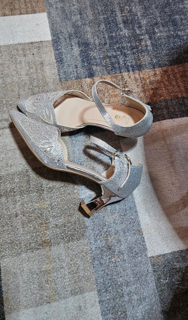 Figlia Silver Glitter Ankle Strap Heels (Category: Heels) located in Dasmarinas. Submitted by jcgshop (Listing ID 1468088206, Image 1). Description: Silver glitter heels from Figlia. Pointed toe design with delicate lace cutouts on the front. Ankle strap with adjustable metal buckle. Shiny metallic heel block, medium height. Neutral beige inner sole. Great option for parties, weddings, or formal events. Minimal wear on the bottom sole..
