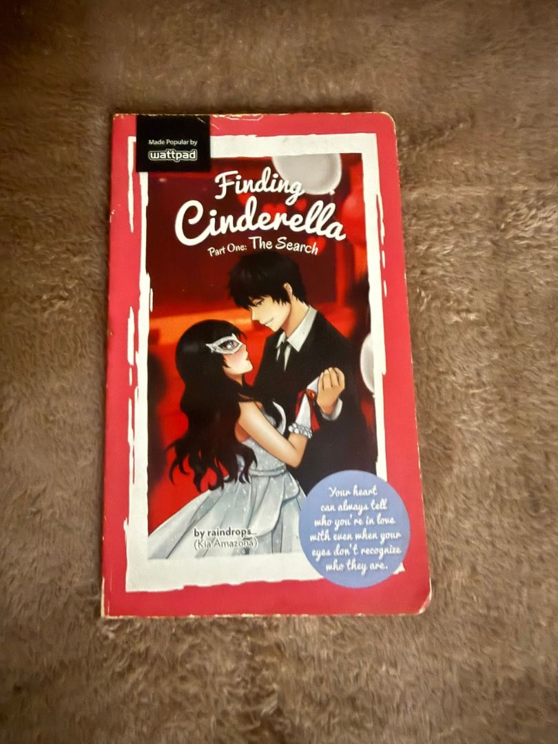 Finding Cinderella Part One: The Search by raindrops (Category: Storybooks) located in Manila. Submitted by bellevuebooks (Listing ID 1468267041, Image 1). Description: Paperback novel titled Finding Cinderella Part One: The Search. Written by raindrops. Made Popular by Wattpad edition. Cover illustration features a couple dancing at an event, with the female character wearing a mask. White border frame design on a red background. Blue circular q