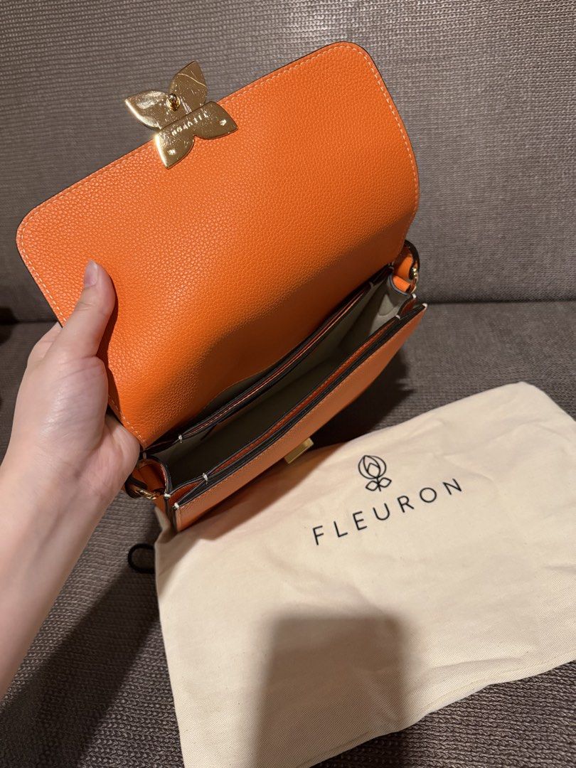 Fleuron Orange Leather Shoulder Bag (Category: Luxury Bags & Wallets) located in General Santos City (Dadiangas). Submitted by mereyelle (Listing ID 1468172980, Image 2). Description: - Brand/Model: Fleuron leather handbag - Color: Bright orange - Hardware: Gold-tone flower clasp closure - Design: Structured body with multiple interior compartments - Strap: Adjustable matching orange leather strap included - Inclusions: Original white cotton dust