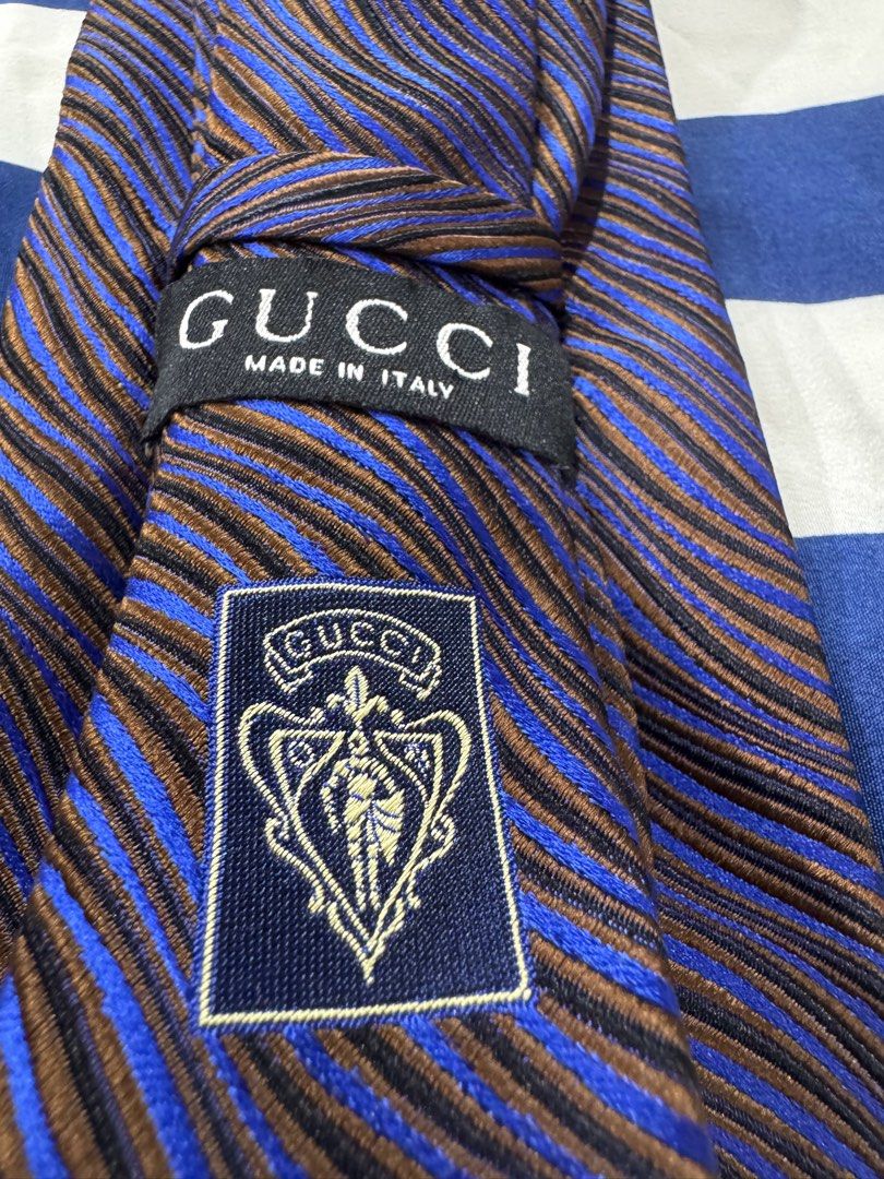 Gucci 100% authentic (Category: Luxury Accessories) located in Manila. Submitted by wildbear.e10374 (Listing ID 1468187345, Image 1). Description: - 100% Authentic Gucci necktie made in Italy - Design: Striking blue, brown, and black wavy stripe pattern with textured fabric - Details: Classic Gucci crest patch and signature woven monogram lining on the interior tail - Condition/Style: Standard men's luxury formal accessory - Perfect for: Business