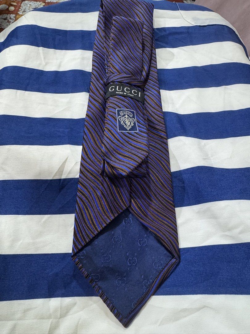 Gucci 100% authentic (Category: Luxury Accessories) located in Manila. Submitted by wildbear.e10374 (Listing ID 1468187345, Image 3). Description: - 100% Authentic Gucci necktie made in Italy - Design: Striking blue, brown, and black wavy stripe pattern with textured fabric - Details: Classic Gucci crest patch and signature woven monogram lining on the interior tail - Condition/Style: Standard men's luxury formal accessory - Perfect for: Business