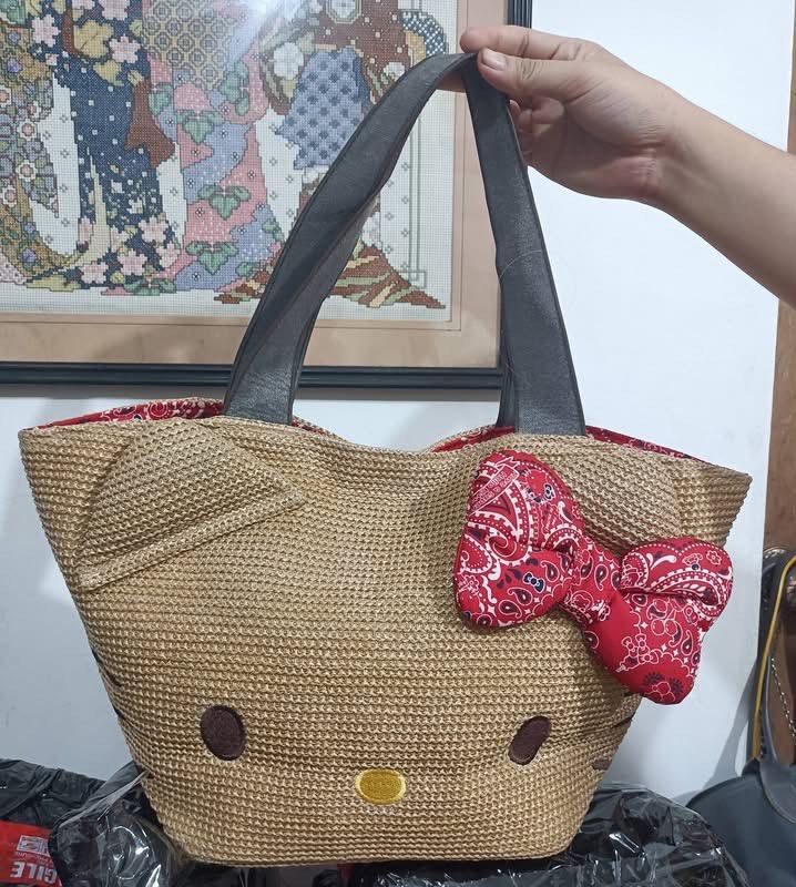 Hello Kitty Straw Tote Bag with Red Bow (Category: Tote Bags) located in Manila. Submitted by janetecson05 (Listing ID 1468215141, Image 1). Description: - Adorable Kitty-shaped straw woven tote bag - Features embroidered eyes and nose with a charming red patterned bow - Equipped with comfortable grey shoulder straps - Styled with a cute red patterned inner lining - Roomy interior, perfect for holding daily essentials - Ideal casual bag for Sanri