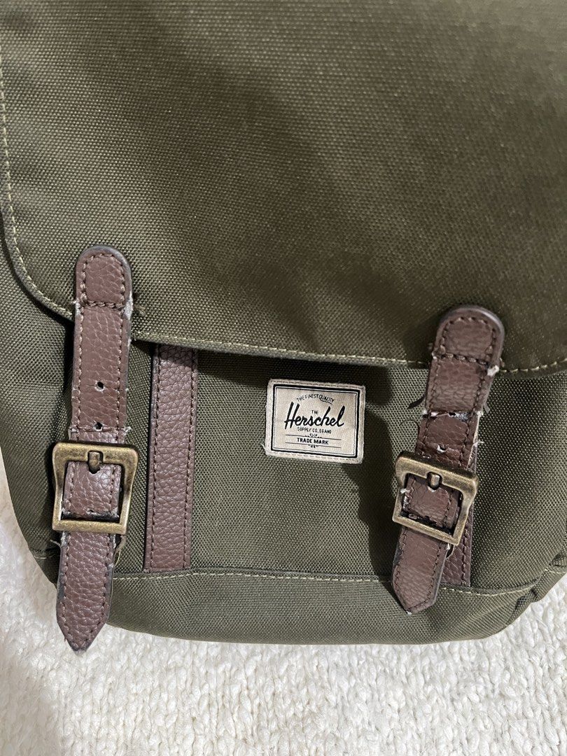 Herschel Green Canvas Backpack (Category: Backpacks) located in Muntinlupa City. Submitted by little.declutter (Listing ID 1468090372, Image 2). Description: - Brand: Herschel Supply Co. - Material: Green canvas with brown faux leather accents - Closure: Drawstring top with magnetic buckle straps - Interior: Signature striped lining - Exterior: Front storage pocket with classic woven brand patch - Condition: Light peeling on the faux leather stra