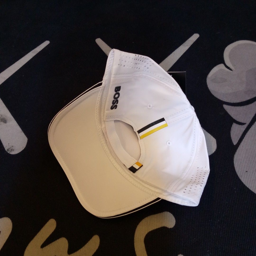 Hugo Boss White Baseball Cap Golf Hat (Category: Caps & Hats) located in Manila. Submitted by pablopresk0. (Listing ID 1468165050, Image 2). Description: - Brand: Hugo Boss - Color: Clean white with dark piping on the brim - Logo: Bold raised BOSS lettering on the front - Comfort: Perforated side panels for enhanced breathability - Fit: Adjustable strap at the back with black and yellow stripe detail - Details: Inner taped seams with repeating BO