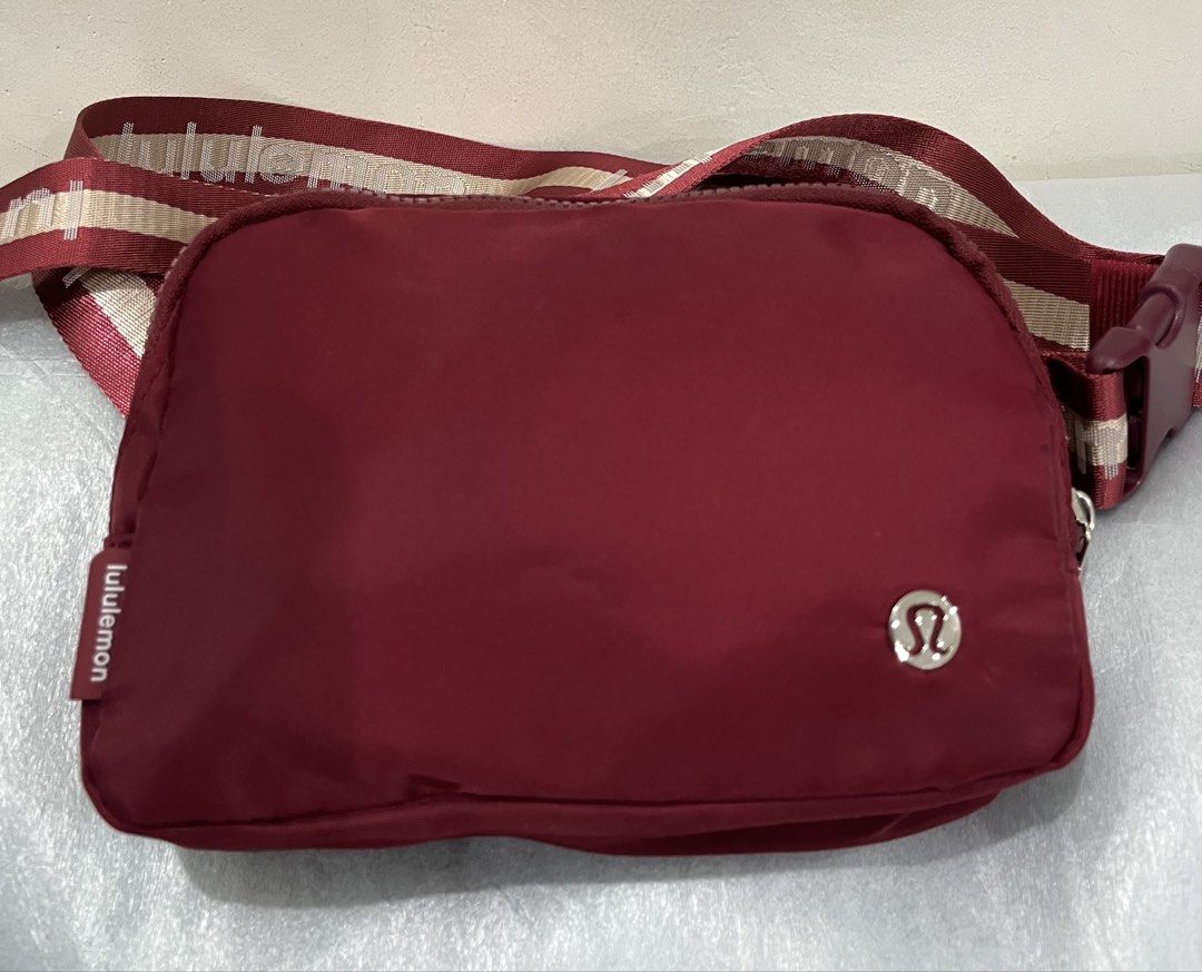 Inspired Lululemon Everywhere Belt Bag with Branded Strap (Category: Cross-body Bags) located in Talisay. Submitted by cherylu (Listing ID 1468267030, Image 1). Description: - Color: Rich burgundy with dark red hardware - Design: Features a trendy striped strap with repeating Lululemon text logo - Branding: Iconic metallic Lululemon logo on the front face - Storage: Secure zippered main compartment with an interior mesh pocket - Details: Clean in