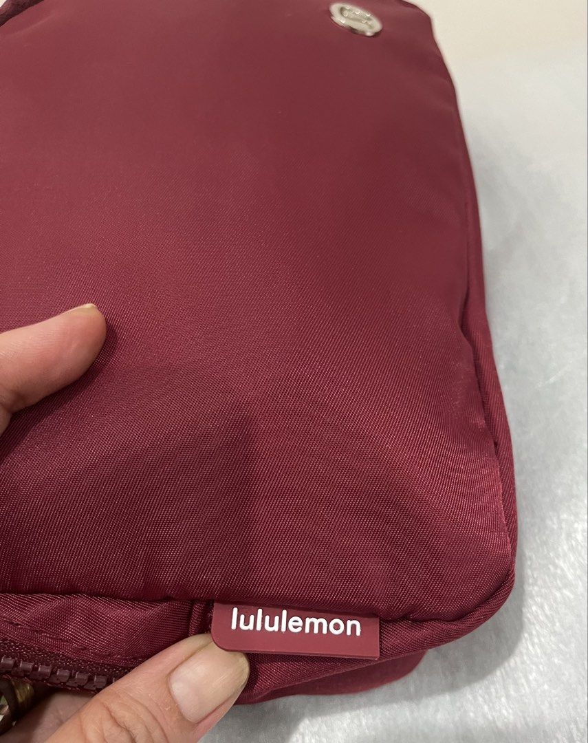 Inspired Lululemon Everywhere Belt Bag with Branded Strap (Category: Cross-body Bags) located in Talisay. Submitted by cherylu (Listing ID 1468267030, Image 2). Description: - Color: Rich burgundy with dark red hardware - Design: Features a trendy striped strap with repeating Lululemon text logo - Branding: Iconic metallic Lululemon logo on the front face - Storage: Secure zippered main compartment with an interior mesh pocket - Details: Clean in