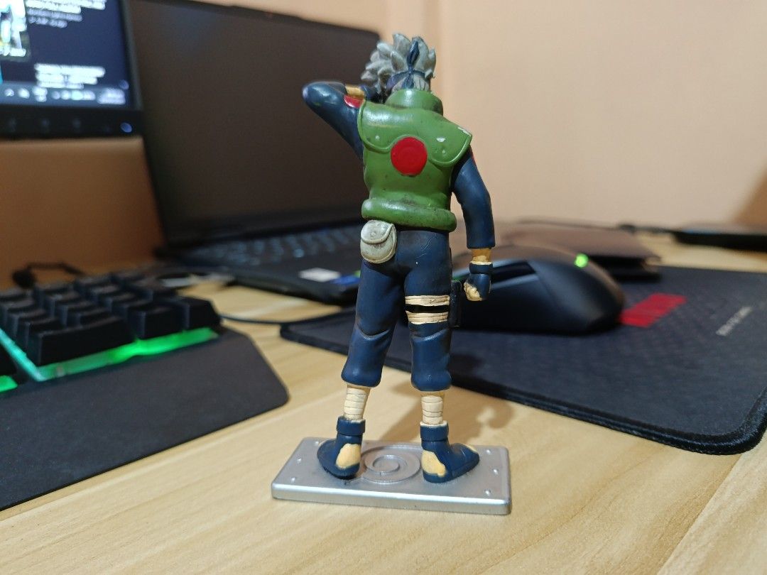 Kakashi Hatake Naruto Anime Figure Statue (Category: Figurines & Statues) located in Ligao. Submitted by travis40 (Listing ID 1468245739, Image 2). Description: - Kakashi Hatake figure from the popular anime series Naruto - Features iconic details: grey hair, green jonin vest, and blue outfit - Dynamic pose with hand raised near the forehead protector - Includes a grey rectangular base with an engraved Leaf Village symbol - Great addition to any 