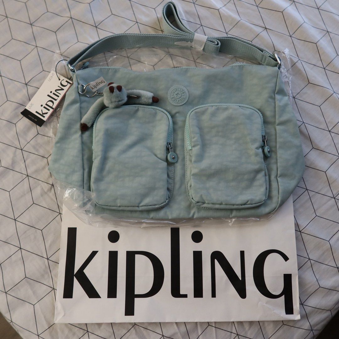 Kipling Sidney Crossbody Bag Springtime Sage (Category: Cross-body Bags) located in Manila. Submitted by gentlewind_62f064 (Listing ID 1468062247, Image 1). Description: - Brand: Kipling - Model: Sidney Crossbody Bag (HB7685 CX1) - Colorway: Springtime Sage - Dimensions: 13.5" x 10" x 6" - Features: Two front zippered compartments and adjustable shoulder strap - Includes: Signature furry monkey keychain named Arianna - Condition: Brand new with o