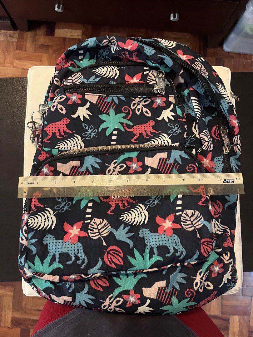 Kipling Tropical Jungle Print Backpack (Category: Backpacks) located in Paranaque City. Submitted by tingar08 (Listing ID 1468137919, Image 3). Description: - Brand: Kipling - Design: Dark blue with vibrant jungle print (pink monkeys, turquoise leopards, palm trees, and tropical flowers) - Compartments: Multiple zippered front pockets for easy organization - Measurements: Approx. 11" wide x 11.5" tall - Hardware: Sturdy zippers with durable metal