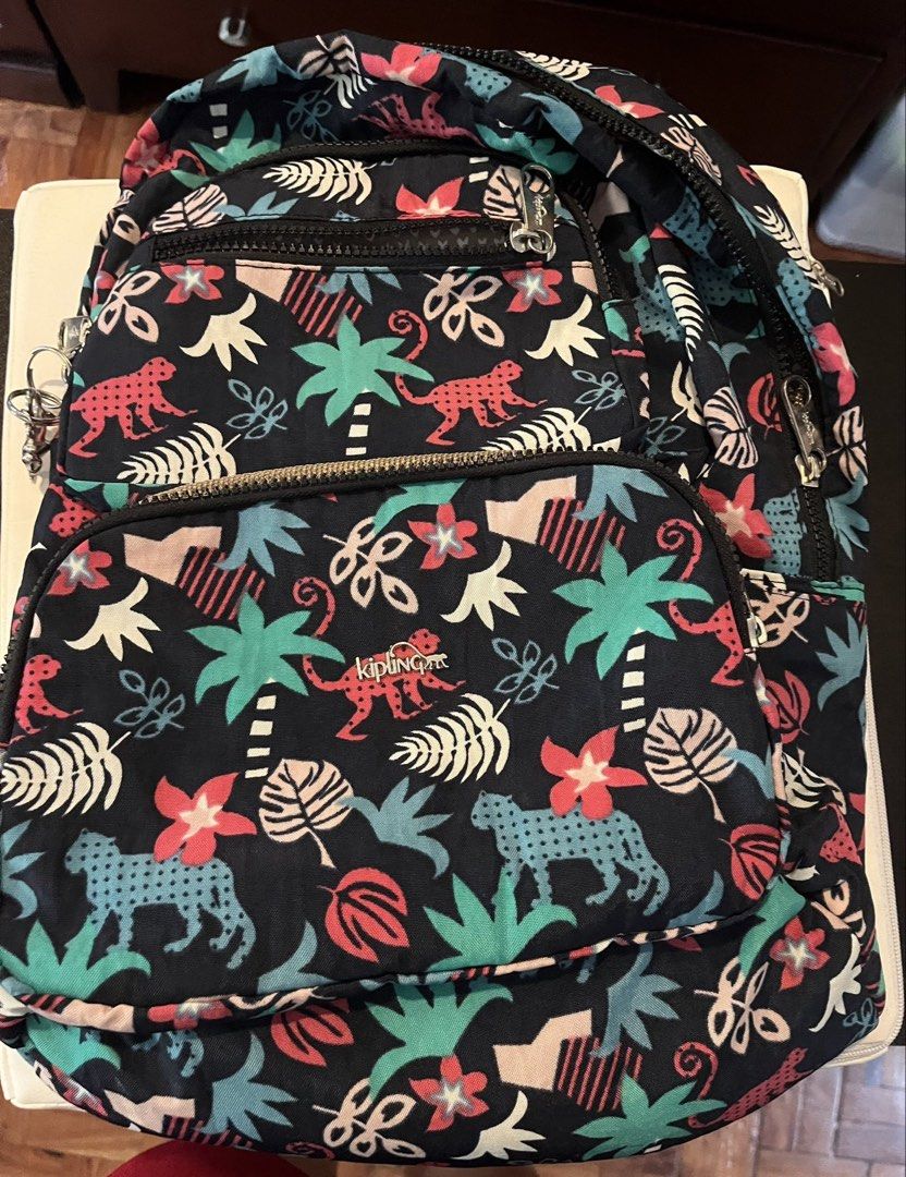 Kipling Tropical Jungle Print Backpack (Category: Backpacks) located in Paranaque City. Submitted by tingar08 (Listing ID 1468137919, Image 1). Description: - Brand: Kipling - Design: Dark blue with vibrant jungle print (pink monkeys, turquoise leopards, palm trees, and tropical flowers) - Compartments: Multiple zippered front pockets for easy organization - Measurements: Approx. 11" wide x 11.5" tall - Hardware: Sturdy zippers with durable metal