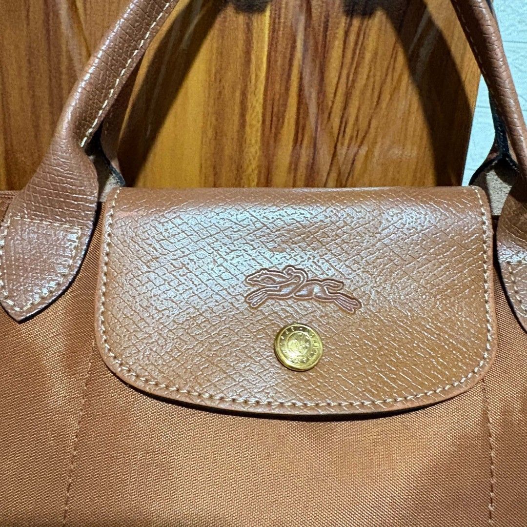 Longchamp Le Pliage Medium Tote Bag Brown (Category: Tote Bags) located in Carmen. Submitted by ar_thrift00 (Listing ID 1468282489, Image 2). Description: - Longchamp Le Pliage Medium Tote in Brown - Durable nylon body with stylish leather handles and flap closure - Elegant gold-tone hardware (zipper pull and snap button) - Stamped interior tag: Longchamp Paris, Made in France - Versatile and spacious for daily commutes, school, or travel - Condi