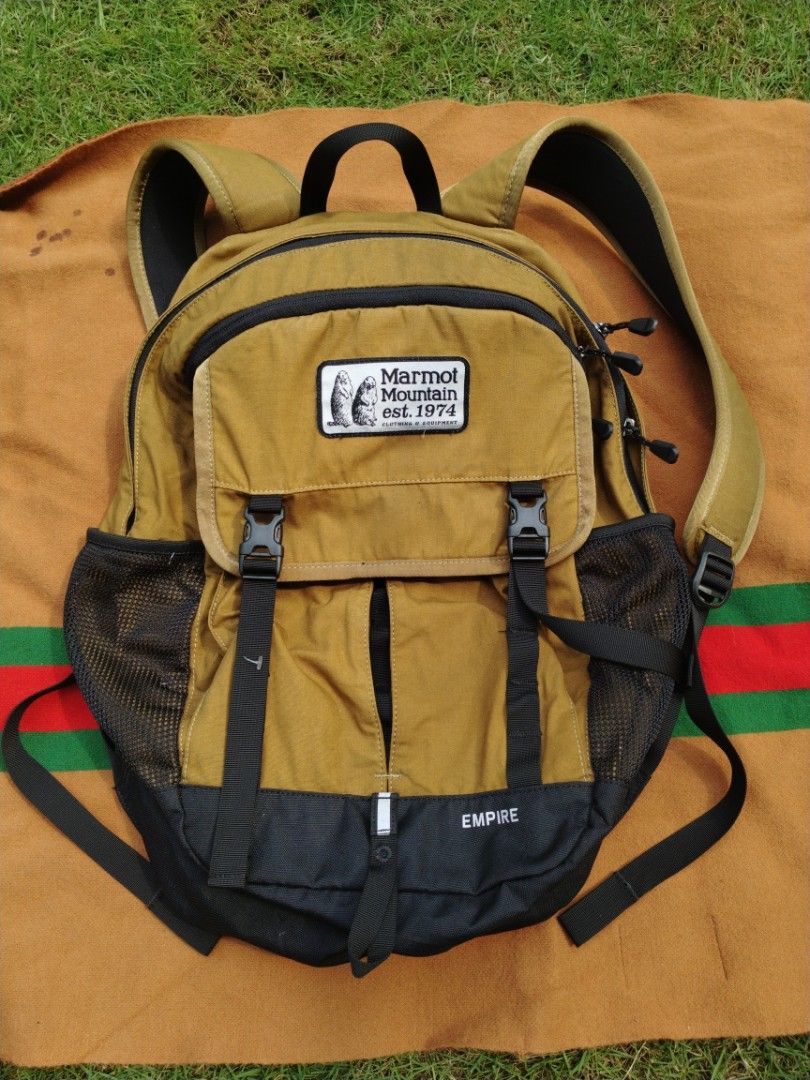 Marmot Mountain Empire Backpack (Category: Backpacks) located in Legazpi City. Submitted by genobecollectives (Listing ID 1468080768, Image 1). Description: - Brand: Marmot Mountain Empire - Color: Mustard Yellow and Black - Design: Front flap with dual buckle straps - Storage: Multiple zippered compartments, interior organizers, and a dedicated laptop sleeve - Pockets: Convenient mesh side pockets - Comfort: Padded back panel and shoulder straps
