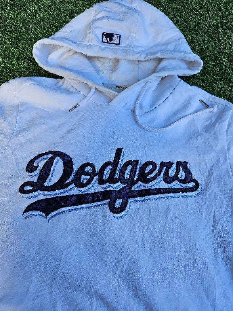 MLB LA Dodgers Hoodie (Category: Hoodies) located in Las Pinas. Submitted by rcp123 (Listing ID 1468144376, Image 2). Description: - Official MLB Genuine Merchandise Los Angeles Dodgers hoodie - Color: White with navy blue and light blue embroidery - Features bold Dodgers team script across the chest - Dodgers diamond patch on left sleeve and MLB batterman logo on the hood - Classic kangaroo pocket, drawstring hood, and official jock tag - Comfor