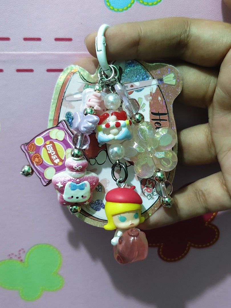 Molly Charms Keychain (Category: Charms) located in Rizal. Submitted by yves1211 (Listing ID 1468258727, Image 1). Description: - Adorable Molly 3D Keychain with multiple charms - Includes a pink Lay's chip bag, pastel angel wings, and a glittery flower accent - Silver-toned hardware with a secure white clasp clip - Great accessory for keys, bags, or backpacks - Adds a fun, personalized touch to your daily items.