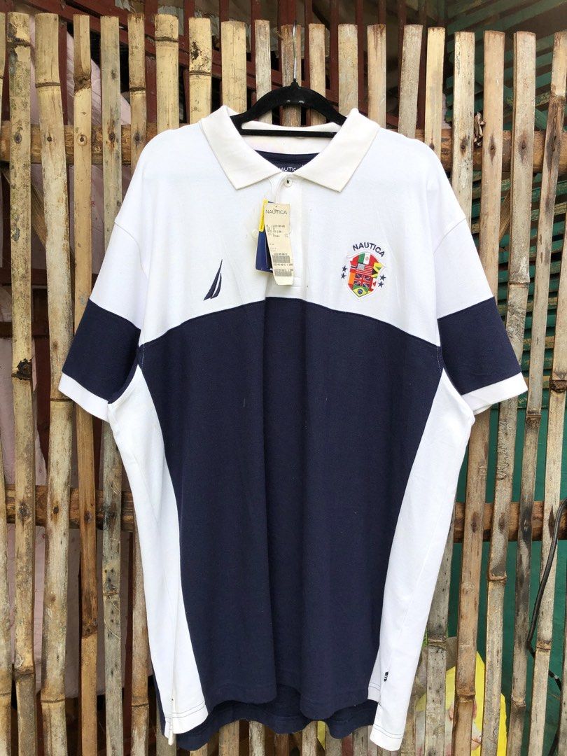 Nautica polo (Category: Tshirts & Polo Shirts ) located in Santa Catalina. Submitted by marlonsecondclosett (Listing ID 1468098141, Image 1). Description: vintage Nautica colorblock short-sleeve polo shirt featuring a white upper half, a navy blue lower half, the “NAUTICA” brand name printed across the back, and a multi-flag shield crest emblem. need wash .