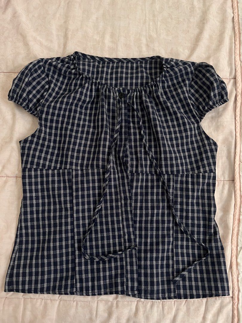 Navy Blue Checkered Short Sleeve Blouse (Category: Blouses) located in Marikina City. Submitted by yeun0923 (Listing ID 1468099621, Image 1). Description: - Navy blue and white plaid pattern - Short puff sleeves with gathered elastic hems - Round neckline with front button closure - Attached long ties at the collar - Flattering empire waistline with panels - Lightweight and breathable cotton-blend fabric - Great for casual everyday styling.