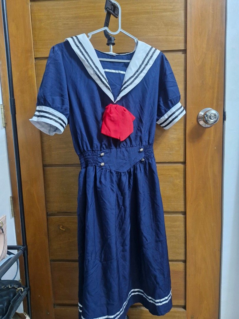 Navy Blue Sailor Dress with Red Bow (Category: Dresses) located in Manila. Submitted by rein.beyaa (Listing ID 1468264373, Image 1). Description: - Color: Navy blue with white and black accents - Style: Sailor dress with short sleeves and mid-length skirt - Details: White collar and sleeve cuffs with double black stripes, smocked waist with front metal buttons - Accessories: Includes a bright red pin-on bow at the chest - Hem: Features matching w