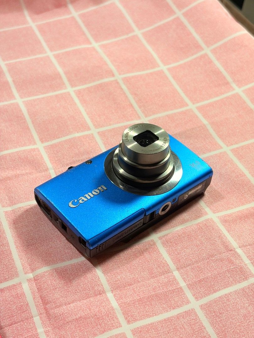 NEGOTIABLE Canon PowerShot A2300 (Category: Cameras) located in Agdangan. Submitted by nakim12 (Listing ID 1468176577, Image 2). Description: - Camera Model: Bright blue Canon digital camera - Resolution & Zoom: 16 megapixels with 5x optical zoom lens - Condition: Fully functional with test shots included; shows minor wear on body paint from regular use - Features: Compact pocket size, side battery/memory card door - Best For: Everyday snaps, str
