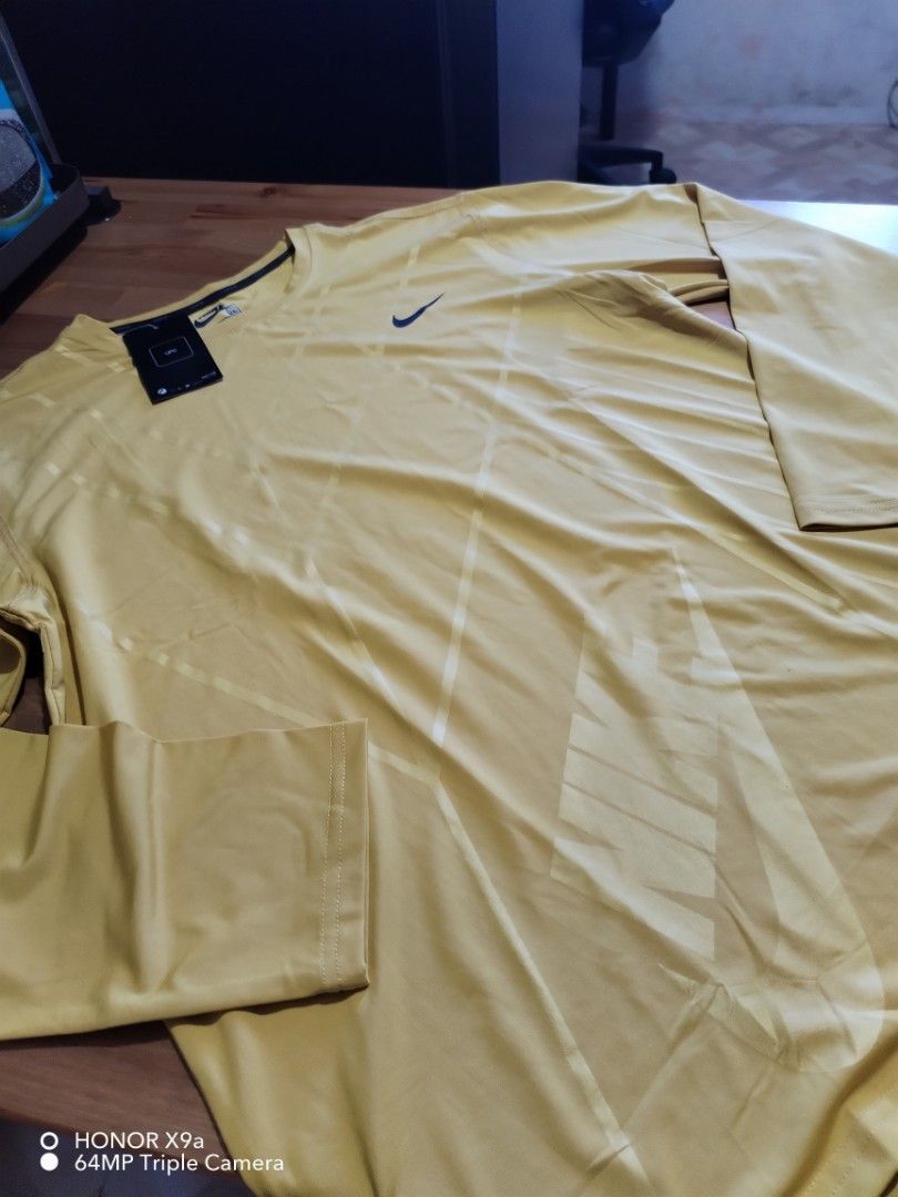 Nike Active Wear (Category: Activewear) located in Muntinlupa City. Submitted by arciagamaryann68 (Listing ID 1468102313, Image 1). Description: - Brand: Nike (Ultimate Tee / Active Wear) - Color: Mustard Yellow with subtle pattern and Nike logo design - Size: 2XL (Tagged 3XL on hang tag) - Material: 100% Polyester with Nike Dri-Fit technology for quick sweat evaporation - Condition: Brand new with tags attached - Features: Long sleeves, lightwei
