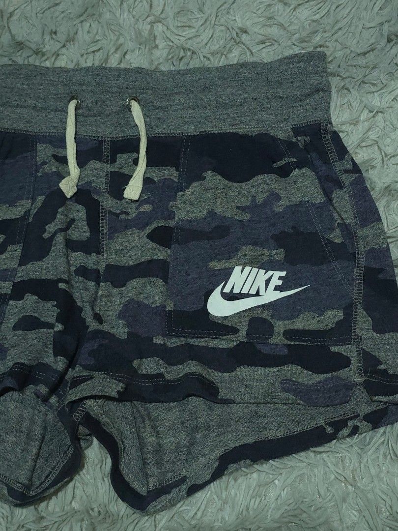 Nike Camo Grey Shorts (Category: Shorts) located in Abulug. Submitted by humanwhosellthings (Listing ID 1468183579, Image 2). Description: NIKE Womens Sweat Short ✅Excellent Condition ✅Issue: none ▫️Waist Size: 30-36 ▫️Length: 11 Grey camouflage Nike shorts with a thick waistband and adjustable drawstring. Pocket on the left leg featuring a large white Nike swoosh and logo print. Blue tag inside reads size L, made in China. Fabric feels soft and 