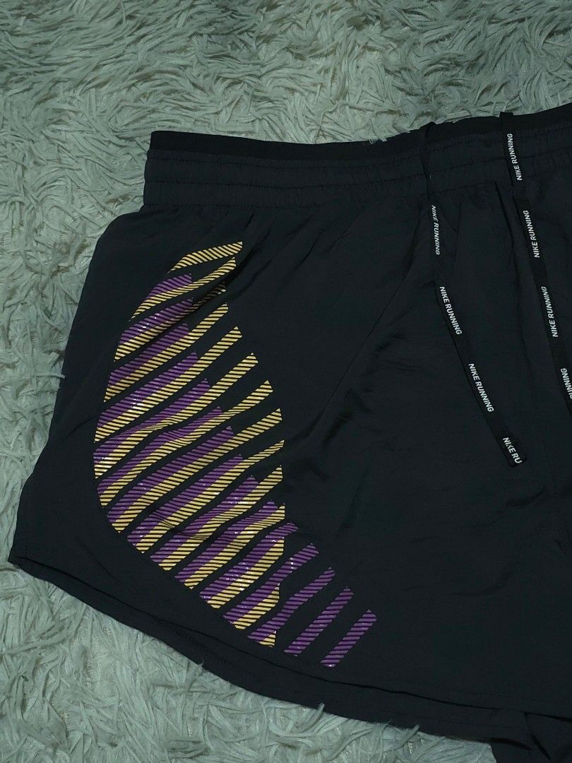 Nike Running Shorts Black With Purple Yellow Pattern (Category: Activewear) located in Abulug. Submitted by humanwhosellthings (Listing ID 1468184726, Image 3). Description: - Brand: Nike ✅Excellent Condition ✅Issue: none ▫️Waist Size: 30-38 ▫️Length: 12 - Color: Black with yellow and purple striped graphic pattern - Fit: Elastic waistband with branded drawstrings - Details: Small reflective swoosh logo on the front leg - Storage: Handy zipped po
