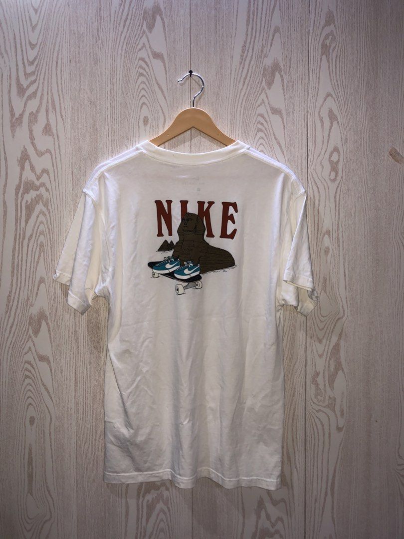 Nike Sphinx Pyramids Graphic T-Shirt White Size M (Category: Tshirts & Polo Shirts ) located in Magsaysay. Submitted by ryns_thrifting (Listing ID 1468165192, Image 2). Description: - Brand: Nike - Style/Model Code: CU0297-100 - Size: Medium - Color: White - Fit: Standard crew neck with short sleeves - Design: Small palm trees and pyramids on the front chest; large Sphinx wearing sneakers on a skateboard graphic on the back with Nike branding - T