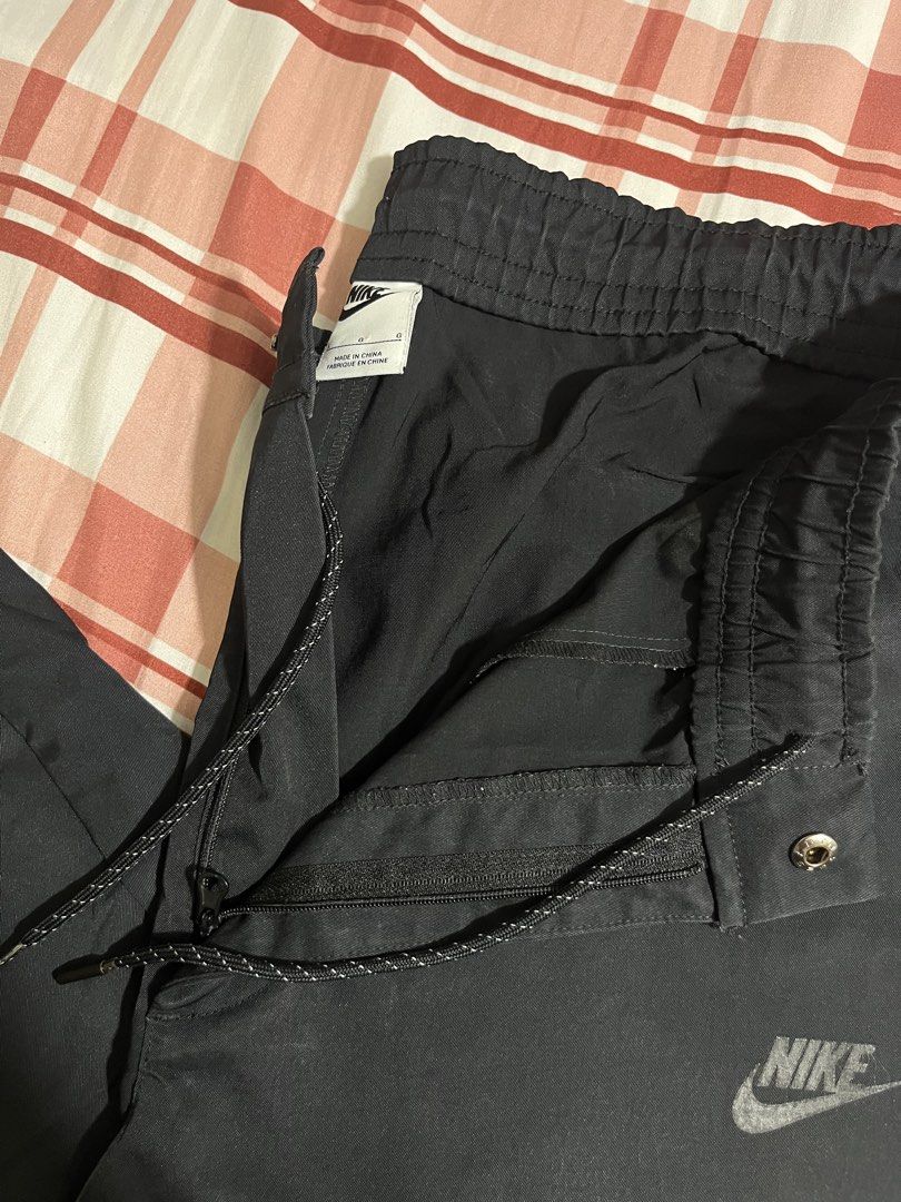 Nike Tech Commuter Casual Pants (Category: Joggers) located in Pasay City. Submitted by Oboyyy (Listing ID 1468090376, Image 2). Description: - Brand: Nike - Color: Black - Size: Large - Waistband: Elastic with stylish patterned drawstrings - Pockets: Convenient zippered side pockets for secure storage - Branding: Subtle Nike logo printed on the leg - Origin: Made in China - Versatility: Great option for workouts, gym sessions, or casual daily we