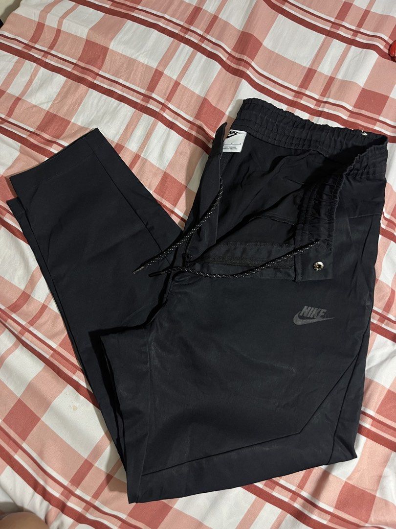 Nike Tech Commuter Casual Pants (Category: Joggers) located in Pasay City. Submitted by Oboyyy (Listing ID 1468090376, Image 1). Description: - Brand: Nike - Color: Black - Size: Large - Waistband: Elastic with stylish patterned drawstrings - Pockets: Convenient zippered side pockets for secure storage - Branding: Subtle Nike logo printed on the leg - Origin: Made in China - Versatility: Great option for workouts, gym sessions, or casual daily we