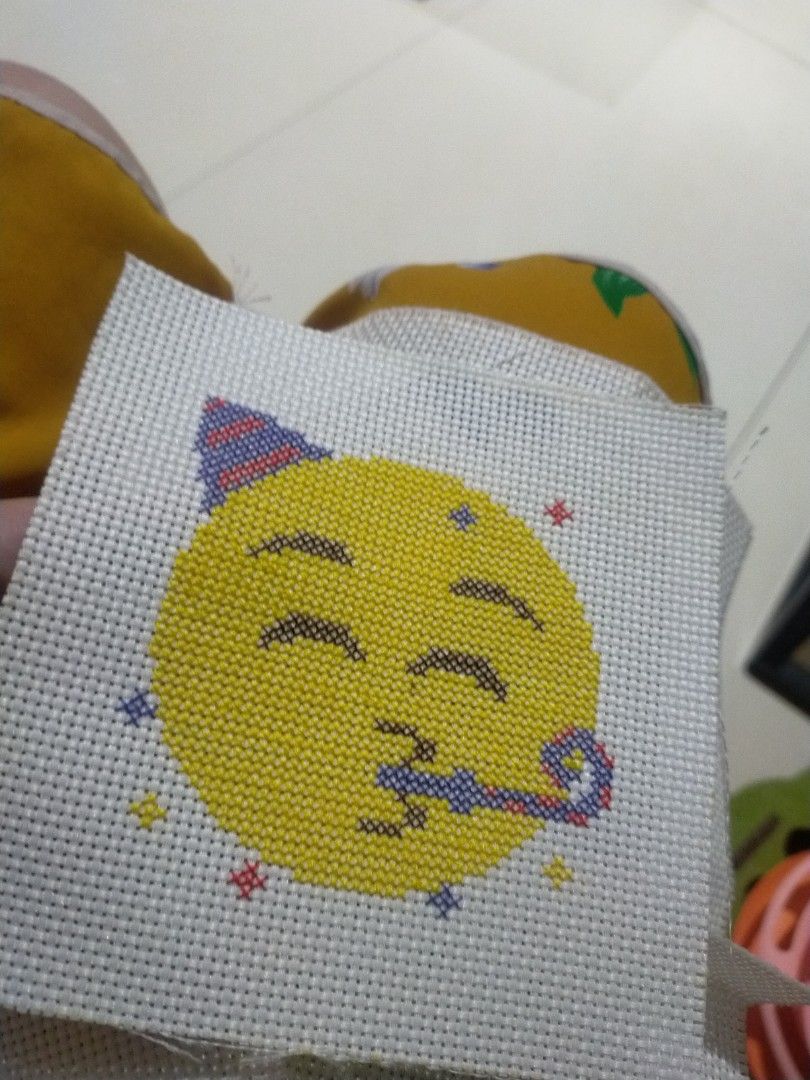 Party emoji cross stitch (Category: Art & Prints) located in Pagadian. Submitted by kimygo (Listing ID 1468158558, Image 1). Description: - Handmade cross stitch project on white aida fabric - Features a 🥳 party emoji, colorful stars, and blue/red patterned accents - Neat and high-quality stitching throughout - Fabric has unfinished edges, ready for custom framing - Perfect gift for craft lovers and home decor enthusiasts.