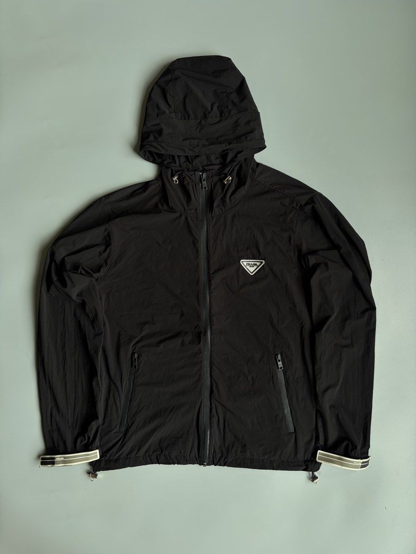 Prada Black Hooded Windbreaker Jacket (Category: Coats, Jackets and Outerwear) located in Kibawe. Submitted by jeloots (Listing ID 1468086000, Image 1). Description: - Authentic Black Prada Hooded Windbreaker (Size L, Made in Italy) - Features iconic rubberized triangle logo patch on the chest - Secure zip closure with zipped front pockets - Adjustable drawstring hood with Prada-stamped metallic hardware - Stylish elastic cuffs with signature bra
