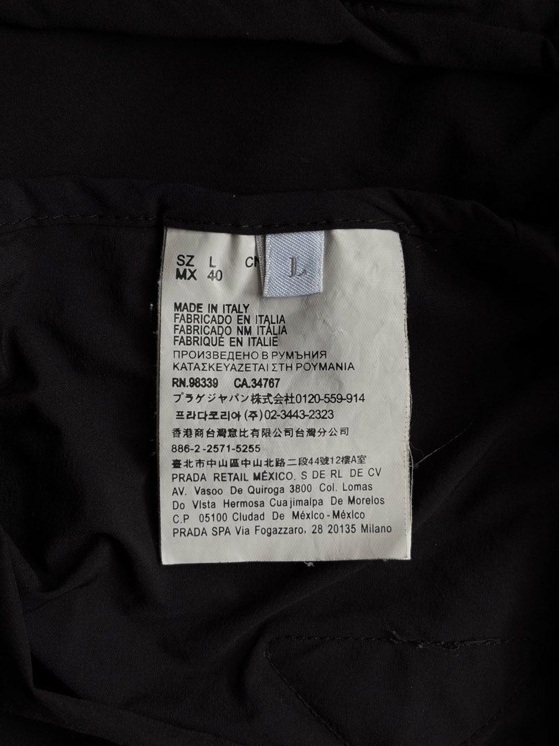Prada Black Hooded Windbreaker Jacket (Category: Coats, Jackets and Outerwear) located in Kibawe. Submitted by jeloots (Listing ID 1468086000, Image 3). Description: - Authentic Black Prada Hooded Windbreaker (Size L, Made in Italy) - Features iconic rubberized triangle logo patch on the chest - Secure zip closure with zipped front pockets - Adjustable drawstring hood with Prada-stamped metallic hardware - Stylish elastic cuffs with signature bra