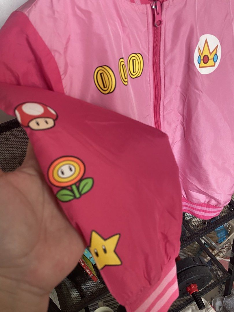 Princess Peach Super Mario Bomber Jacket Pink (Category: Babies & Kids Fashion) located in Las Pinas. Submitted by dhyn29 (Listing ID 1468158361, Image 3). Description: - Authentic Super Mario Princess Peach pink bomber jacket - Convenient front zipper closure with striped ribbed cuffs and collar - Princess Peach crown logo on the chest with coin and Mario/Peach graphics near the hem - Sleeves feature iconic mushroom, fire flower, and star power-