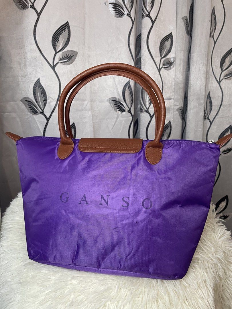 Purple GANSO Tote Bag – Stylish & Spacious (Category: Tote Bags) located in Cabanatuan. Submitted by moraiahraven (Listing ID 1468146537, Image 3). Description: Brand: GANSO Colour: Vibrant purple with brown handles & trim Material: Lightweight nylon body + leather handles & flap Features: • Classic foldable-style tote design • Dual brown top handles • Zip-top closure with branded metal pull • Front flap with gold-tone snap button + embossed GANS