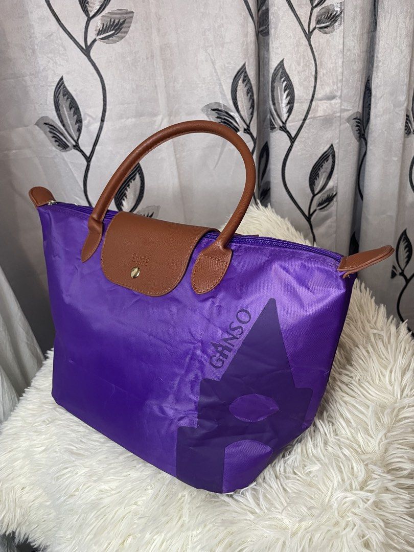Purple GANSO Tote Bag – Stylish & Spacious (Category: Tote Bags) located in Cabanatuan. Submitted by moraiahraven (Listing ID 1468146537, Image 2). Description: Brand: GANSO Colour: Vibrant purple with brown handles & trim Material: Lightweight nylon body + leather handles & flap Features: • Classic foldable-style tote design • Dual brown top handles • Zip-top closure with branded metal pull • Front flap with gold-tone snap button + embossed GANS