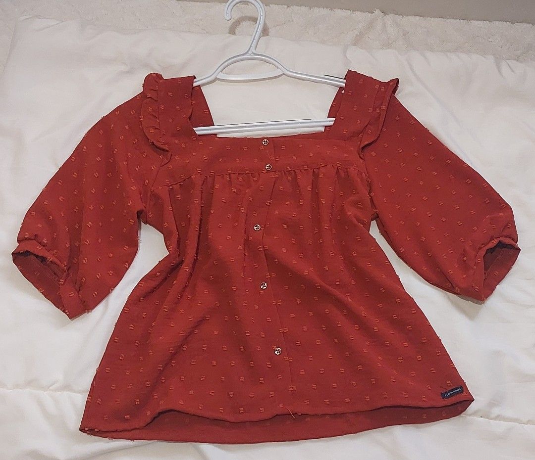 Crissa Swiss Dot Square Neck Blouse with Ruffled by Straps (Category: Blouses) located in Pasig City. Submitted by salazaralona (Listing ID 1468066813, Image 1). Description: - Color: Rusty red with all-over dotted texture - Neckline & Straps: Square neckline with playful ruffled shoulder straps - Sleeves: Half sleeves - Closure: Functional front button closure - Details: Gathered yoke across the chest - Material: Lightweight and breathable - Sty