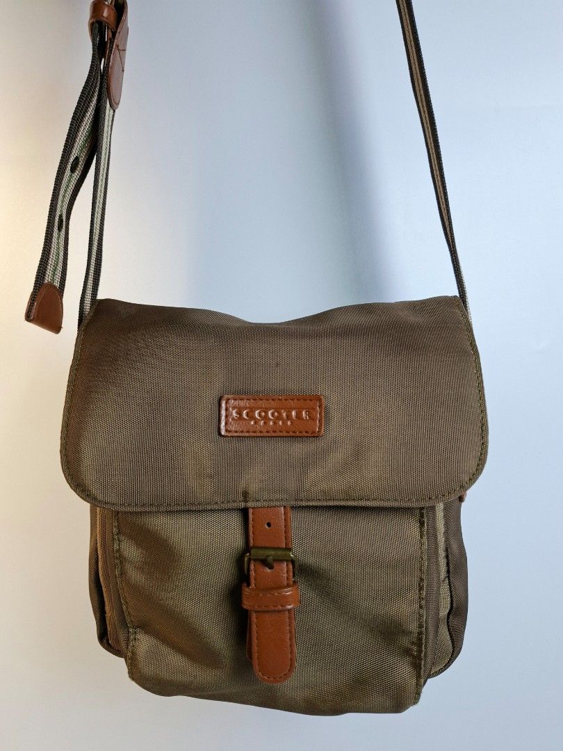 Scooter Brown Nylon Crossbody Bag (Category: Cross-body Bags) located in Pasay City. Submitted by onick_79 (Listing ID 1468251218, Image 1). Description: -Dimensions: L23 x H23 x 12 cm - Color: Brownish-green with brown leather-look accents - Material: Durable nylon - Strap: Adjustable striped strap with buckle detail - Closure: Front flap with strap and metal buckle - Storage: Extra zipper pocket on the back for easy access - Size: Compact and i