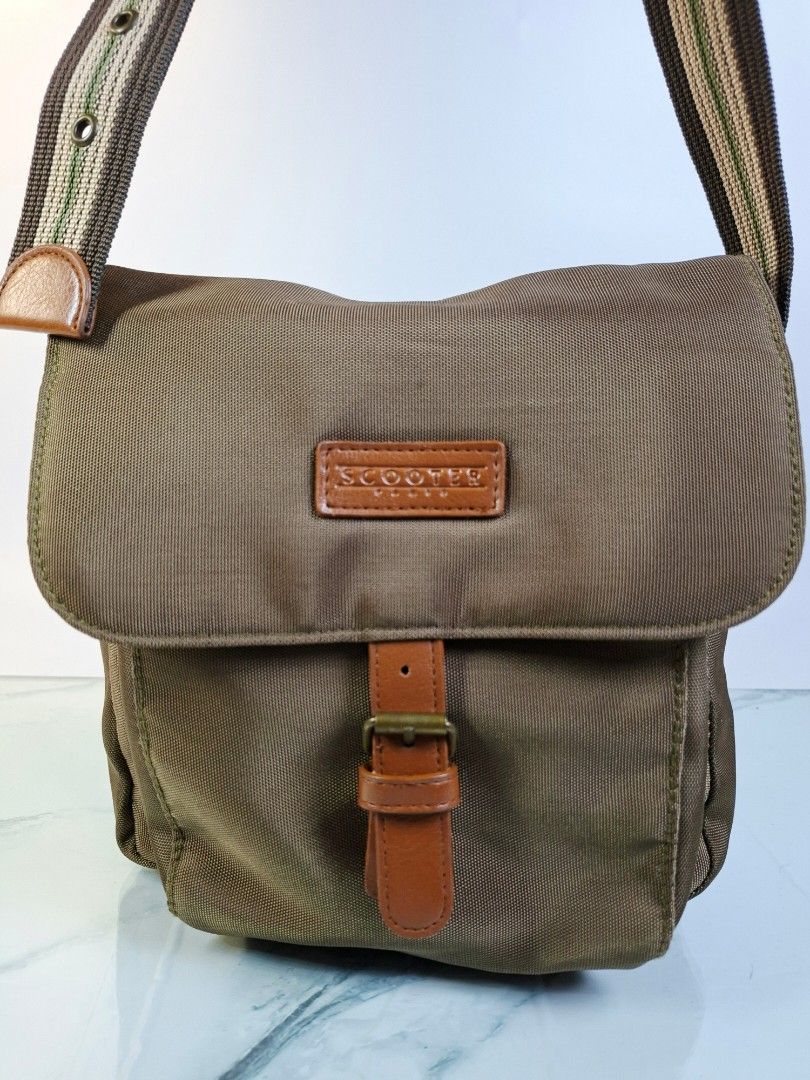 Scooter Brown Nylon Crossbody Bag (Category: Cross-body Bags) located in Pasay City. Submitted by onick_79 (Listing ID 1468251218, Image 3). Description: -Dimensions: L23 x H23 x 12 cm - Color: Brownish-green with brown leather-look accents - Material: Durable nylon - Strap: Adjustable striped strap with buckle detail - Closure: Front flap with strap and metal buckle - Storage: Extra zipper pocket on the back for easy access - Size: Compact and i