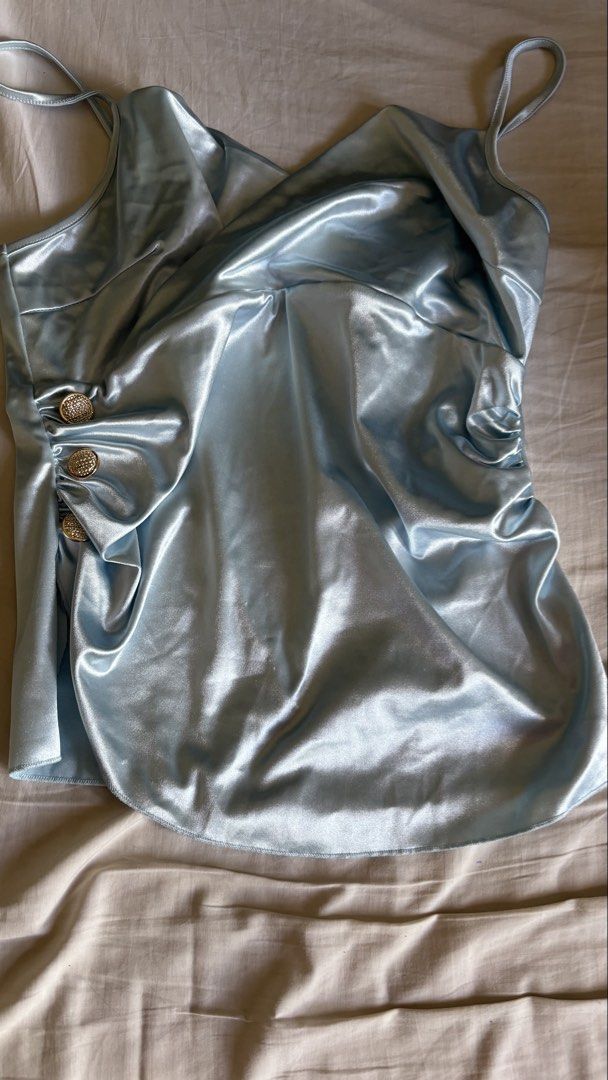 Shein Silk Satin Light Blue Cowl Neck Top (Category: Sleeveless) located in Binan City. Submitted by myprelovedhaul (Listing ID 1468070216, Image 3). Description: The image shows a light blue satin-style camisole featuring a cowl neckline, thin shoulder straps, side ruched detailing, and decorative buttons along the gathered side seam. Similar styles are commonly found on online retailers like Temu and SHEIN as ruched or pleated cami tops with bu