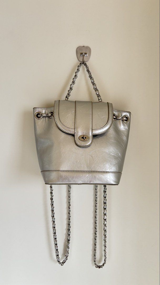 Silver metallic mini backpack with chain straps (Category: Backpacks) located in Baguio. Submitted by zenforest.fd186d (Listing ID 1468224986, Image 2). Description: Silver metallic mini backpack with a crinkled texture. - Twist-lock closure on the front flap. - Chain straps and top handle in silver-tone hardware. Inside is lined with striped fabric and includes a small slip pocket. - Hardware has a few minor scuffs, but overall clean shape..