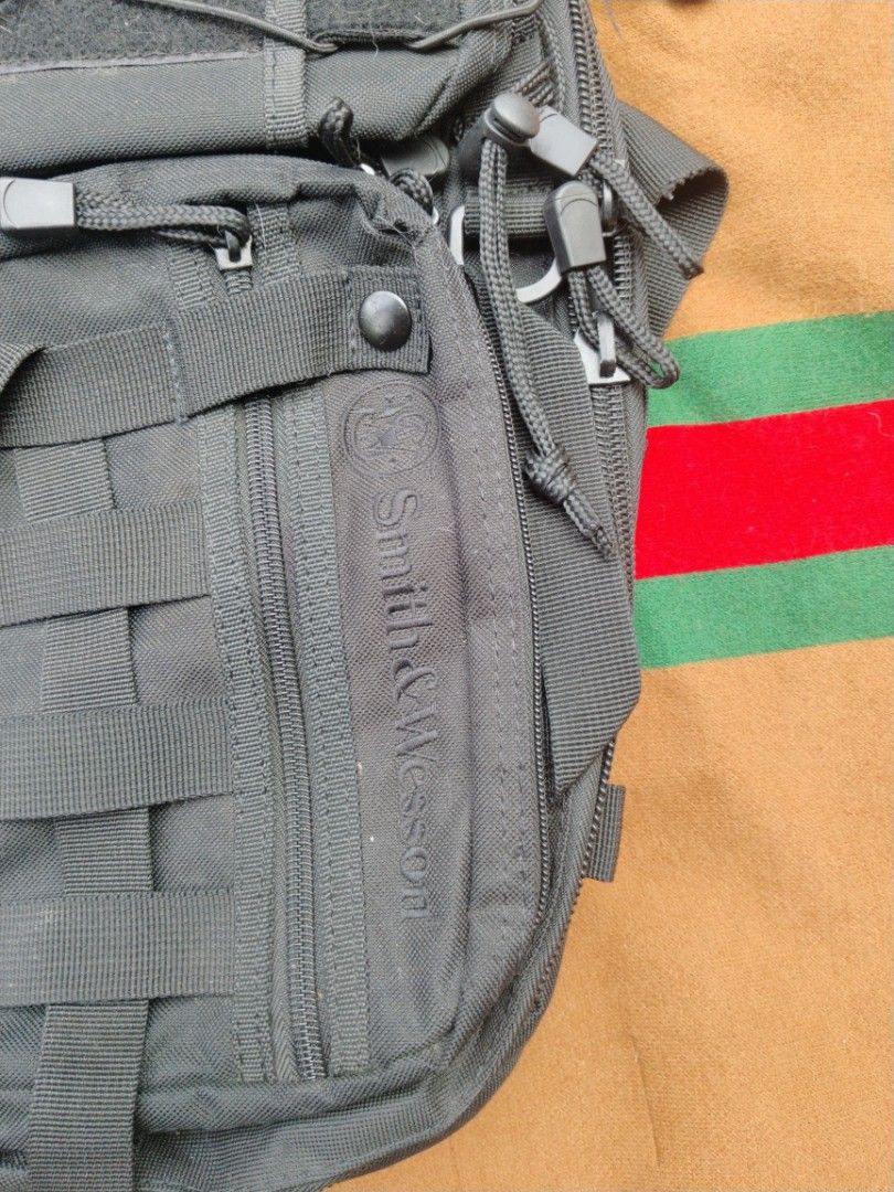 Smith & Wesson tactical sling backpack black (Category: Sling Bags) located in Legazpi City. Submitted by genobecollectives (Listing ID 1468080919, Image 3). Description: Smith & Wesson tactical sling backpack in all black. Durable nylon material with heavy-duty zippers and paracord pulls. Multiple exterior zippered compartments, MOLLE webbing straps, and bungee cords on the front pocket. Padded mesh back panel and single adjustable shoulder stra