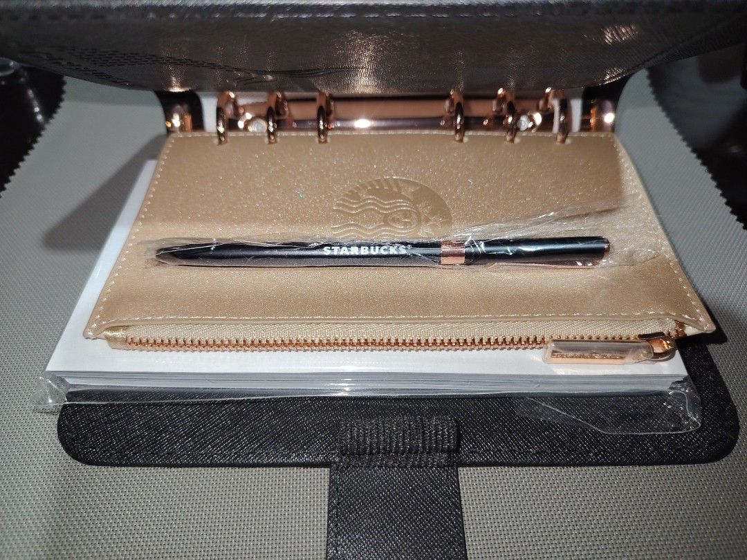 Starbucks 2023 Planner (Category: Stationery & School Supplies) located in Manila. Submitted by storageninjaph (Listing ID 1468144140, Image 3). Description: - Authentic Starbucks 2023 Planner in Black and Rose Gold - Six-ring binder style for easy customization - Includes a matching gold glittery zipper pouch - Comes with a brand new, sealed Starbucks black and rose gold pen - Brand new and unused; snap button closure still has original protecti
