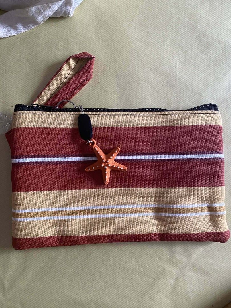 Striped Beach Pouch with Starfish Charm (Category: Purses & Pouches) located in Zaragoza. Submitted by sherree1281 (Listing ID 1468282751, Image 1). Description: - Color: Red, beige, and white stripes - Material: Durable canvas - Closure: Secure zipper with cute orange starfish charm - Features: Includes a convenient wrist strap - Use: Perfect for carrying small essentials on a day out.